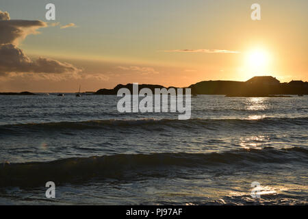 Coucher de soleil sur la baie de Trearddur près de Holyhead, Rivier, au nord du Pays de Galles avec la lumière du soleil qui se reflète sur l'eau et des vagues. Ciel Orange paysage seasc silhouette Banque D'Images