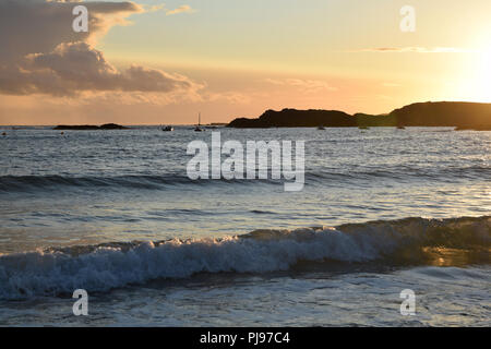 Coucher de soleil sur la baie de Trearddur près de Holyhead, Rivier, au nord du Pays de Galles avec la lumière du soleil qui se reflète sur l'eau et des vagues. Ciel Orange paysage seasc silhouette Banque D'Images