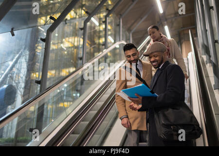 Businessmen discussing paperwork sur escalator urbain de nuit Banque D'Images