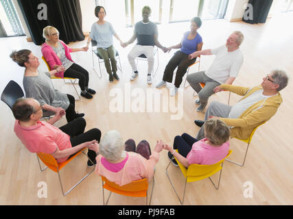 Les aînés actifs holding hands in circle, méditant dans community centre Banque D'Images