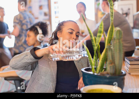 Businesswoman arrosage cactus avec de l'eau bouteille in office Banque D'Images