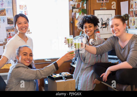 Portrait confiant creative designers femelle vert potable smoothies en office Banque D'Images