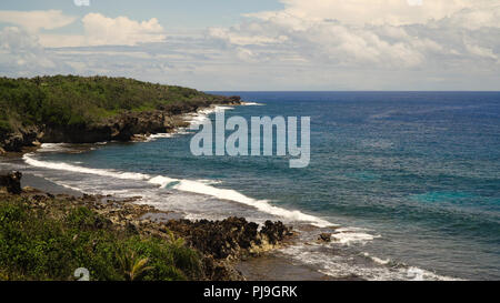 Plage de rochers avec des palmiers, le bleu de l'eau sur une île tropicale. La côte rocheuse de la mer, vagues se brisant sur la côte rocheuse. Point de vue le long de plage de galets avec des pierres.Stony mer plage scène. Aux Philippines. Concept de voyage. Banque D'Images