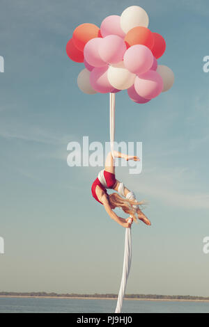 Jeune fille fait de cascades audacieuses et acrobatiques. Elle flotte dans l'air sur des ballons. Banque D'Images