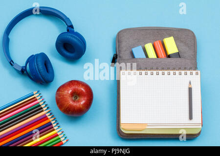 Crayons de couleur, apple, écouteurs, ouvrez un livre d'exercices sur-sac à crayons-feutres de couleur et marqueur sur fond bleu. Vue d'en haut. Retour à l'école c Banque D'Images