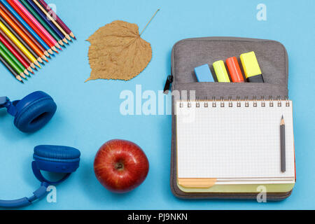 Écouteurs, crayons de couleur, apple, feuille sèche, ouvrez un livre d'exercices sur-sac à crayons-feutres de couleur et marqueur sur fond bleu. Vue d'en haut. Retour t Banque D'Images