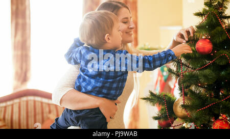 Tonique portrait of smiling young woman avec son petit garçon babioles hanging on Christmas Tree Banque D'Images