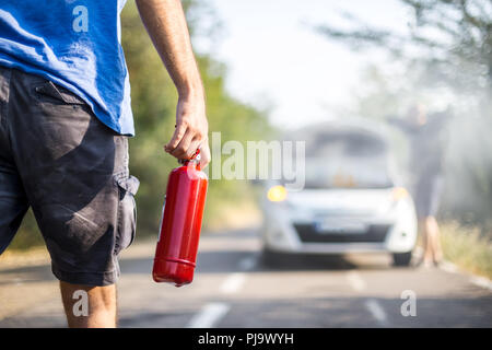 Homme avec un extincteur d'aider une personne avec une voiture à la flamme Banque D'Images