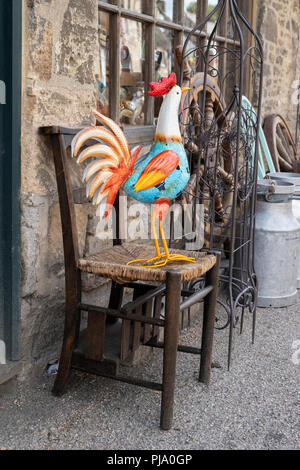 Coq en métal coloré sur une chaise en bois à l'extérieur et boutique d'antiquités à Lechlade on Thames, Gloucestershire, Angleterre Banque D'Images