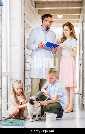 Montrant quelque chose dans le presse-papiers de vétérinaire à femme, enfants jouant avec le pug chien à la clinique vétérinaire Banque D'Images