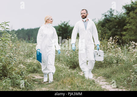 Les hommes et les scientifiques dans des scaphandres de marcher avec valise de travail et presse-papiers dans le pré Banque D'Images