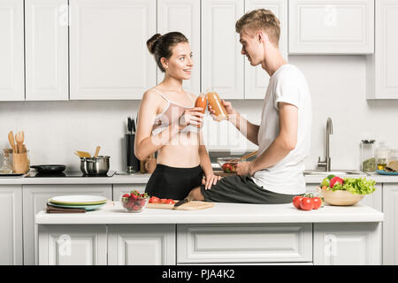 Jeune couple de trinquer avec des bouteilles de jus sains dans la cuisine Banque D'Images