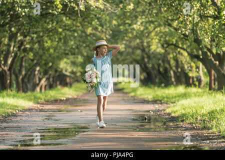 Belle enfant de sexe féminin dans le quartier branché de robe et chapeau de paille holding bouquet de fleurs et la marche en verger Banque D'Images