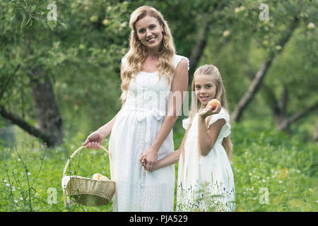 Belle Mère et fille holding panier en osier avec des fruits dans un verger Banque D'Images