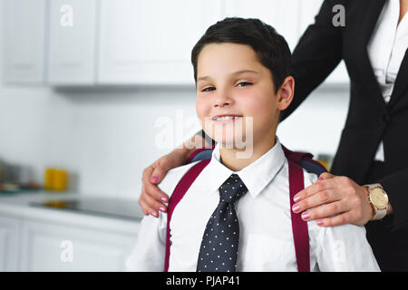 Vue partielle de mère en costume et fils dans l'uniforme scolaire avec sac à dos dans la cuisine à la maison, concept retour à l'école Banque D'Images