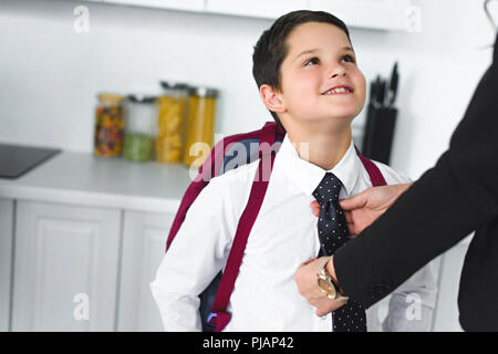 Vue partielle de mère en fils de liage en costume cravate cuisine à la maison, concept retour à l'école Banque D'Images