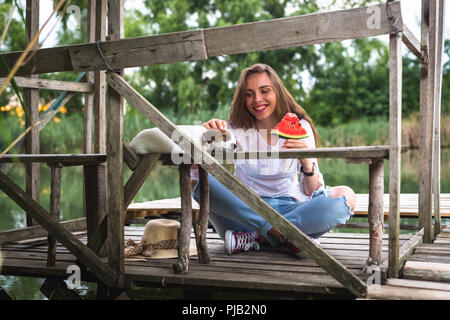 Femme avec son animal de compagnie sur le quai de la rivière eating watermelon Banque D'Images