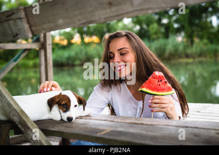 Femme avec son animal de compagnie sur le quai de la rivière eating watermelon Banque D'Images