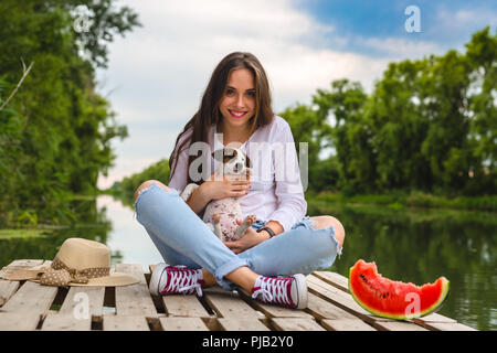 Couple de l'été avec son chiot , assis sur le quai de la rivière Banque D'Images