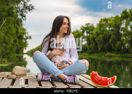 Couple de l'été avec son chiot , assis sur le quai de la rivière Banque D'Images