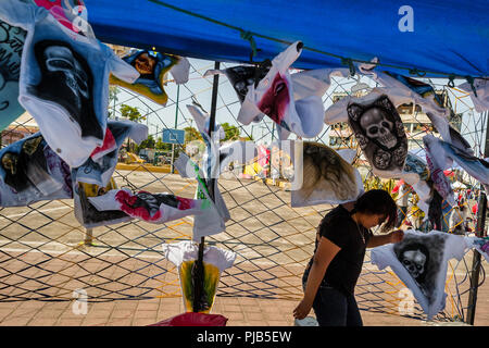 Une jeune femme mexicaine vend des t-shirts, avec divers Santa Muerte (sainte mort) images, dans la rue au cours d'un pèlerinage dans la ville de Mexico, Mexique. Banque D'Images