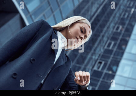 Femme regardant sa montre-bracelet en allant à l'office de consultation sur l'arrière-plan de la ville Banque D'Images