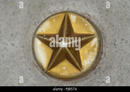 Un beau gros plan d'une étoile à cinq branches sur un cercle de métal intégré dans le béton. La couleur or pâle un peu. Banque D'Images