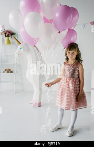 Smiling anniversaire enfant tenant bouquet de ballons et debout avec unicorn décoratif Banque D'Images