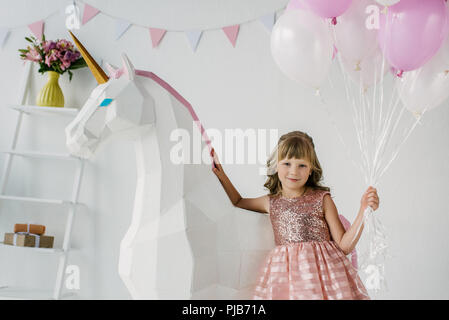 Adorable petit kid holding bouquet de ballons et debout avec unicorn décoratif Banque D'Images