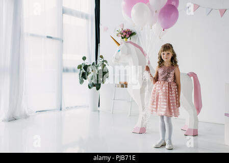 Anniversaire kid holding bouquet de ballons et debout avec unicorn décoratif Banque D'Images