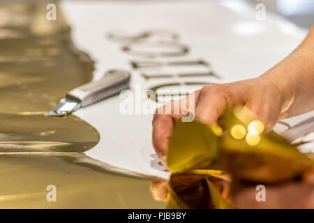 Décoration de Noël découper à partir d'un brillant or imprimer. Jeune femme travaillant avec une précision de coupe à main. Banque D'Images