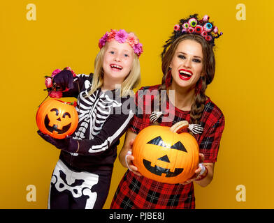 Halloween colorés. smiling mother and daughter moderne de style mexicain costume halloween sur fond jaune montrant jack-o-lanterne citrouille Banque D'Images