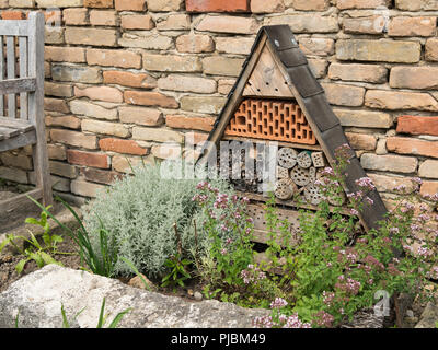 Un hôtel des insectes, debout devant un mur de brique dans un jardin avec diverses plantes Banque D'Images