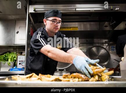 Océan Pacifique (12 juillet 2018) - Spécialiste culinaire Seaman Derrick Williams, de Piketon, Ohio, lieux les pommes de terre sur une plaque à pâtisserie avant le déjeuner à bord du destroyer lance-missiles USS Dewey (DDG 105). Dewey est en cours participant à l'exercice Rim of the Pacific (RIMPAC). Vingt-cinq nations, 46 navires, 5 sous-marins, environ 200 avions et 25 000 personnes participent à l'EXERCICE RIMPAC du 27 juin au 2 août dans et autour des îles Hawaï et la Californie du Sud. Le plus grand exercice maritime international RIMPAC, fournit une formation unique tout en renforçant et en s Banque D'Images