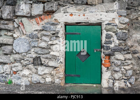 Petite porte en bois vert verrouillé avec un cadenas sur un vieux mur de pierre grise Banque D'Images