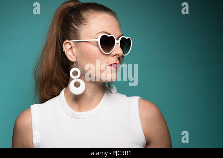 Un cheveux roux Caucasian woman en queue de cheval, portant un mod 60s style sungalsses en forme de coeur et d'oreilles, posant un portrait en gros plan. Banque D'Images