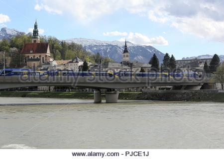 Un tramway passe sur un pont au centre-ville de Salzbourg sur une soirée ensoleillée, avec les Alpes en arrière-plan. Banque D'Images