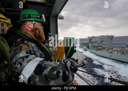 En mer (19 juillet 2018) de la Royal Australian Navy Matelot maître de Manœuvre Zackary Kelly, de Sydney, les signaux de l'hélicoptère du navire de débarquement quai HMAS Adelaide (L01) de la Marine royale du navire MV Astérix lors d'un ravitaillement en mer au cours de Rim of the Pacific (RIMPAC), le 19 juillet. Vingt-cinq nations, 46 navires, 5 sous-marins, et d'environ 200 avions et 25 000 personnes participent à l'EXERCICE RIMPAC du 27 juin au 2 août dans et autour des îles Hawaï et la Californie du Sud. Le plus grand exercice maritime international RIMPAC, fournit un ensemble unique de trai Banque D'Images