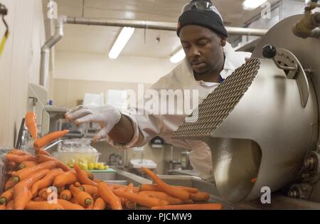 Jason Griffin, Travail Services Corp., spécialiste de la transformation des aliments supprime les carottes à partir d'une machine qui lave les légumes et enlève la peau extérieure en préparation de repas à Sheppard Air Force Base, Texas, le 17 juillet 2018. La cuisine Préparation à la Sheppard des milliers de livres de légumes, viandes et autres ingrédients et articles quotidiennement dans le cadre du processus de la base de fournir plus de 10 000 repas aux aviateurs, marins, soldats, marins et les étudiants internationaux des cours ici. Banque D'Images