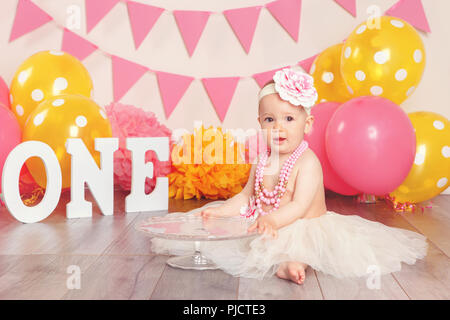 Portrait of cute adorable Caucasian baby girl in tutu jupe en tulle célèbre son premier anniversaire. Enfant kid sitting on floor en studio avec drapeaux rose Banque D'Images