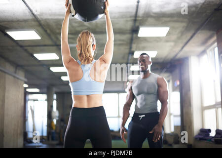 Trainer regarder female client ascenseur medicine-ball in gym Banque D'Images