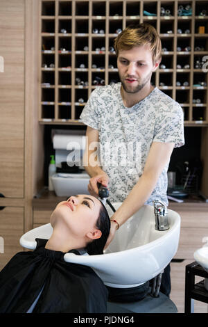 Coiffure homme lave-tête client. Un homme maître de cheveux cheveux de la fille d'un arrosage avec une douche dans un salon de coiffure. Banque D'Images