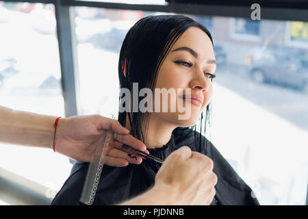 Coiffure homme faire une coupe pour une belle fille brune dans le salon de coiffure professionnel. Banque D'Images