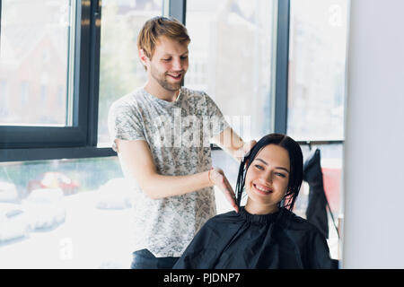 Coiffure homme sourire et parler avec un client tout en faisant une nouvelle coupe de belle jeune femme brune Banque D'Images