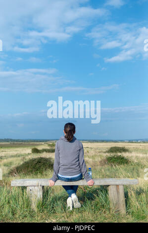 Vue arrière d'une femme assise sur un banc en bois à la campagne à. Banque D'Images