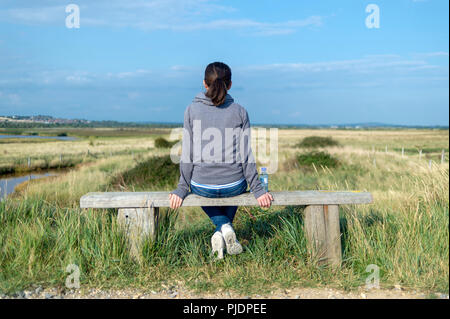 Vue arrière d'une femme assise sur un banc en bois à la campagne à. Banque D'Images