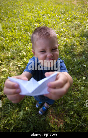 Maintenez l'enfant rire heureux navire papier à l'intérieur. Champ vert arrière-plan. Enfance heureuse, été, vacances, voyages, vacances Banque D'Images