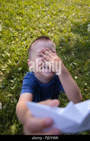 Maintenez l'enfant rire heureux navire papier à l'intérieur. Champ vert arrière-plan. Enfance heureuse, été, vacances, voyages, vacances Banque D'Images