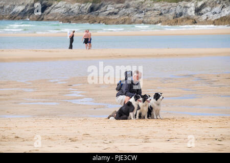 Un homme à genoux avec ses trois chiens Border Collie sur plage de Crantock en Newquay Cornwall. Banque D'Images