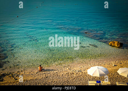 L'homme est assis dans le silence et le calme à l'aube au bord de l'eau de la mer Adriatique au village de Baska, sur l'île croate de Krk Banque D'Images